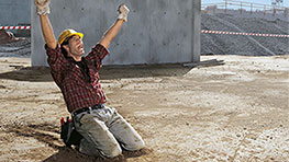 A construction worker kneels on the ground and cheers with joy.