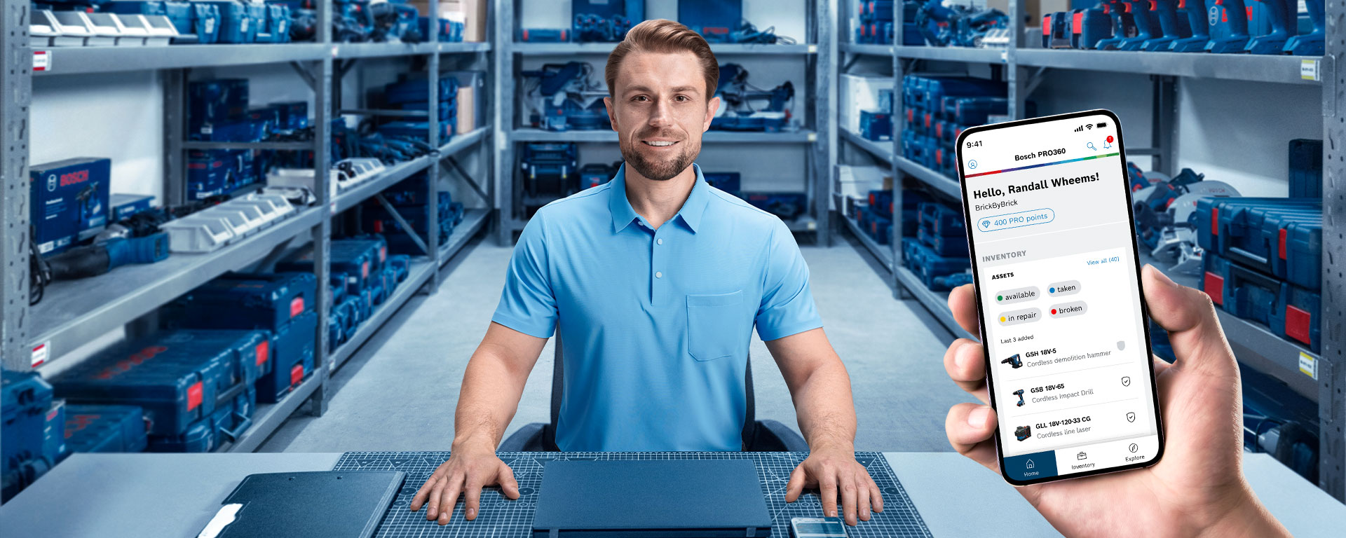 A man in a blue shirt is sitting at a table in a warehouse with tools in the background.