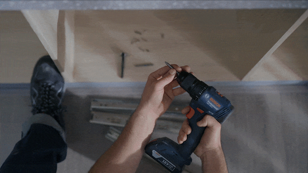 FOR YOUR REQUIREMENTS A person holds a blue Bosch Professional cordless drill over wood.