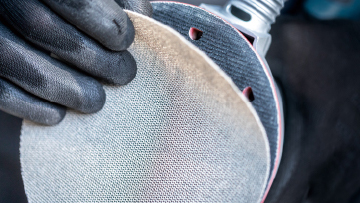 A hand holds a Bosch Professional grinding disc with holes.