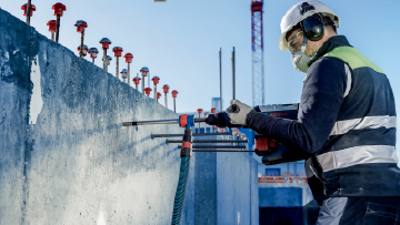 A worker with a helmet is drilling into a concrete wall at a construction site.