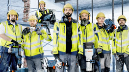 Six construction workers in yellow helmets and safety vests are standing on a construction site.