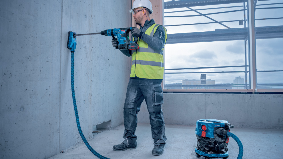 A man with a helmet and vest is drilling into a concrete wall.