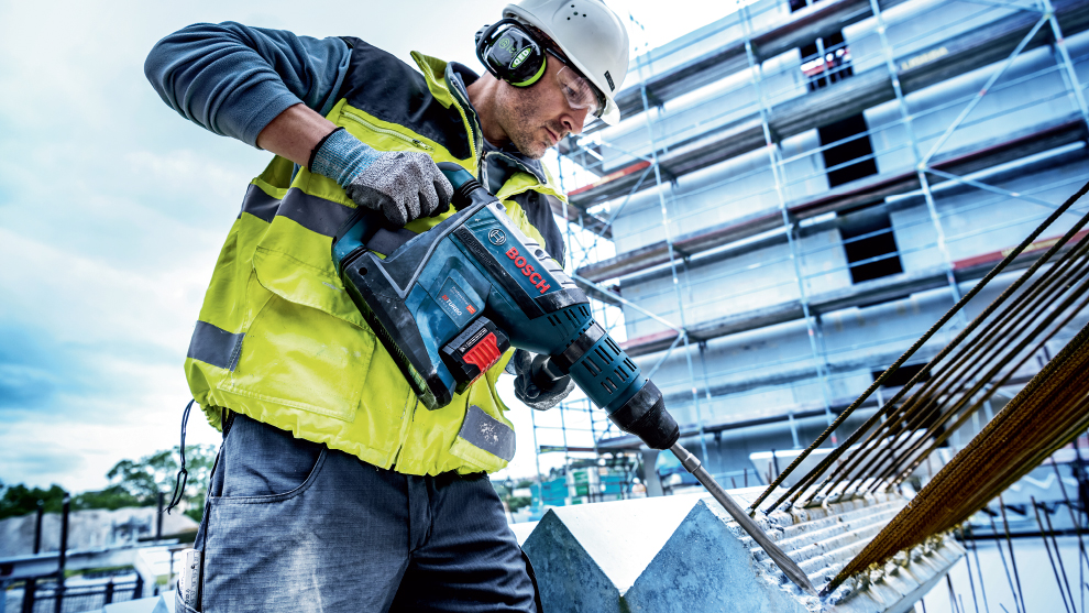 A worker with Bosch tools is drilling into a concrete block at a construction site.