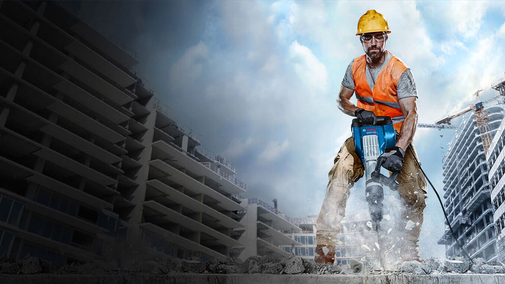 A man wearing a hard hat and orange vest is working with a Bosch hammer.