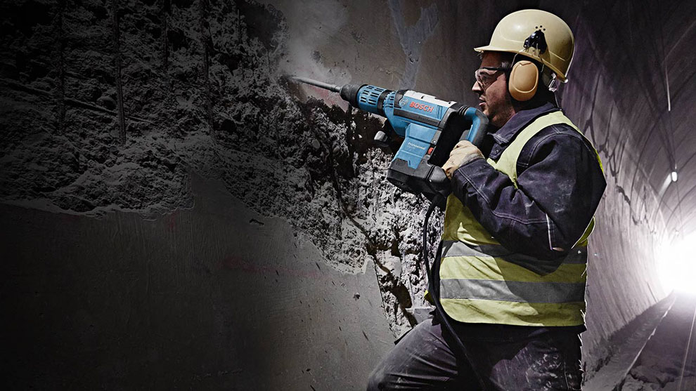 A worker with a Bosch hammer drill is breaking a wall in a tunnel.