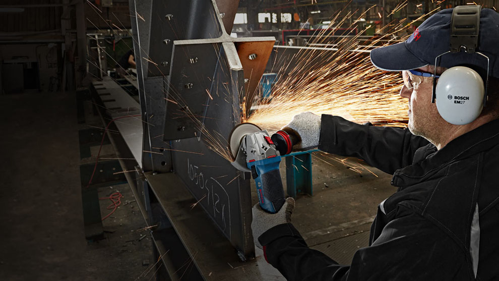 A man is cutting metal with a blue Bosch tool. Sparks are flying.