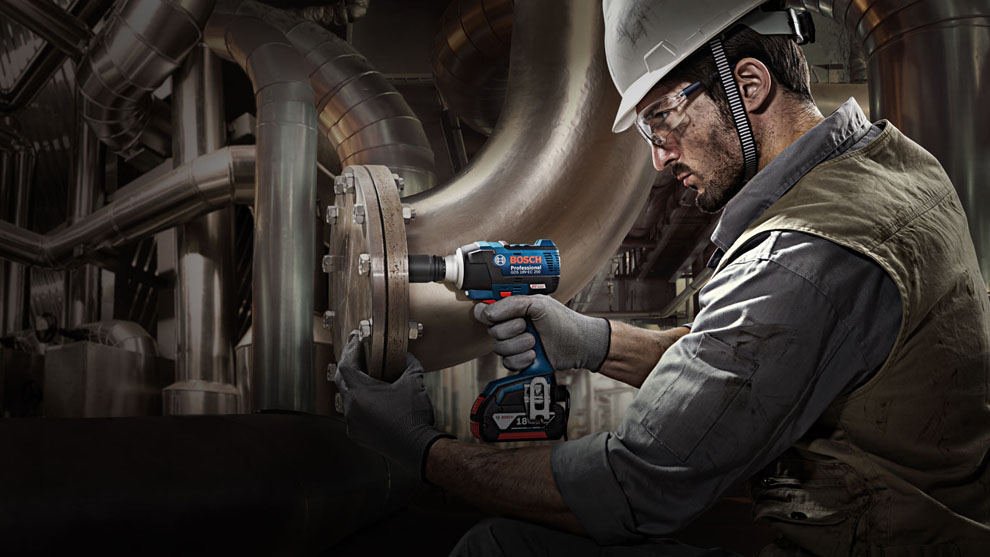 A man with a helmet is using a blue Bosch Professional cordless drill.