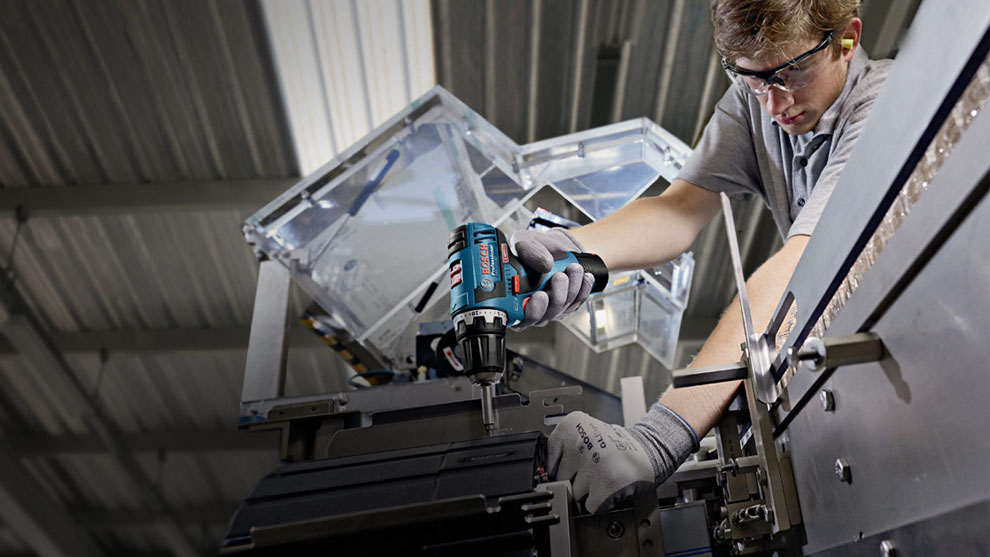 A worker is using a Bosch Professional cordless screwdriver in a workshop.