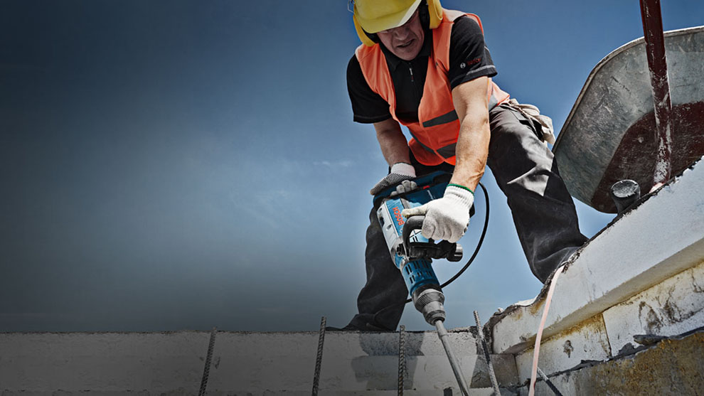 Worker in safety vest with Bosch hammer drill on construction site.