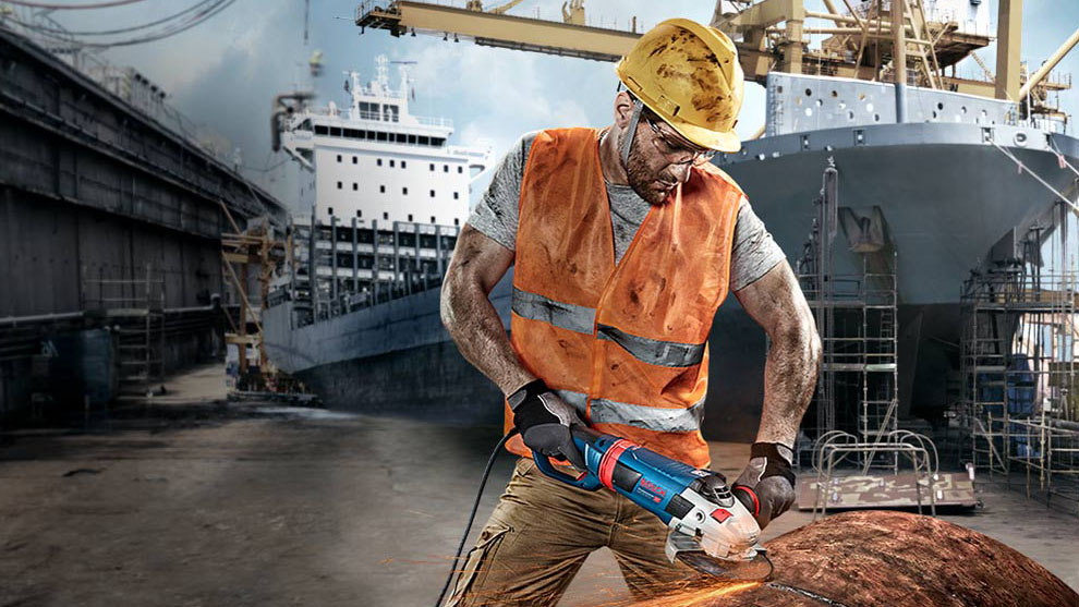 A worker wearing a safety helmet is cutting metal with a blue Bosch machine.