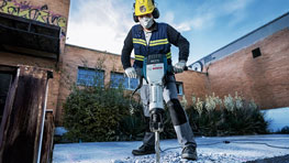 A worker with a helmet operates a Bosch demolition hammer on concrete.