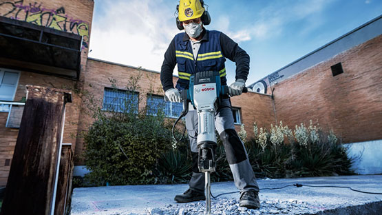 A worker with a Bosch hammer is working on concrete outdoors.