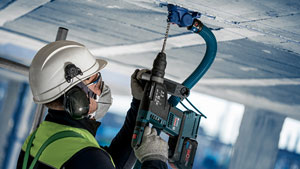 A worker with a helmet is drilling into the ceiling with a Bosch Professional tool.