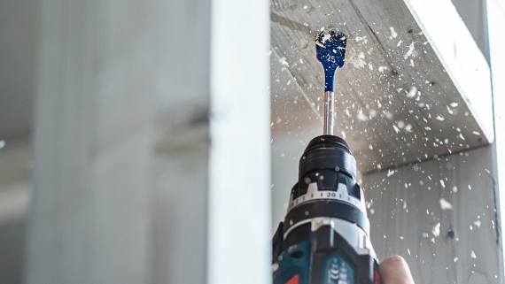 A Bosch Professional cordless drill is drilling into a piece of wood, shavings are flying.