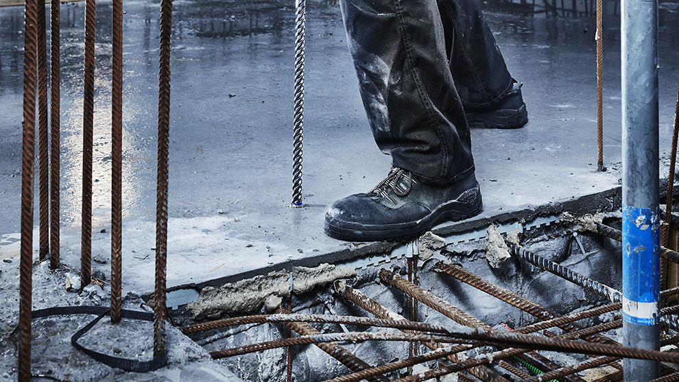 A worker in black boots stands on a concrete surface.