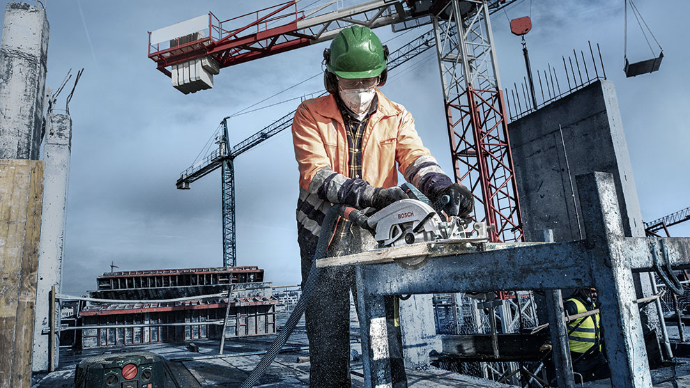 A worker with a green helmet is cutting wood with a Bosch saw at the construction site.