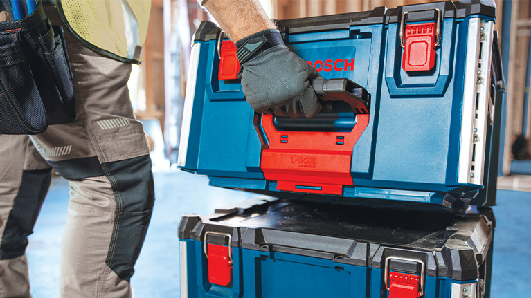 A craftsman lifts a blue toolbox with red accents from a stack.