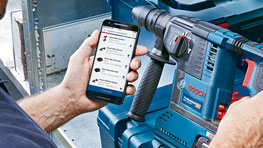 A person is using a smartphone next to a blue Bosch Professional tool.